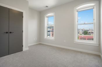 A room with a grey carpet, a grey door and a window with a view of the city.